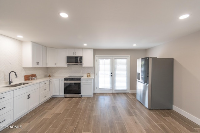 kitchen featuring sink, tasteful backsplash, light hardwood / wood-style flooring, appliances with stainless steel finishes, and white cabinets