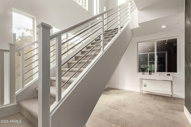 staircase featuring recessed lighting, baseboards, and a towering ceiling