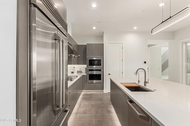 kitchen with a sink, light countertops, under cabinet range hood, appliances with stainless steel finishes, and modern cabinets