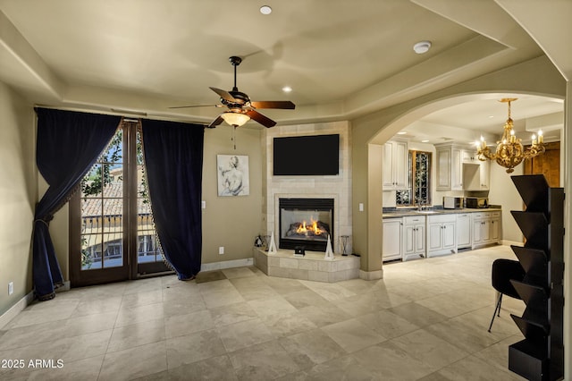 10894 E Turquoise Ave, Scottsdale, AZ 85259 - unfurnished living room with baseboards, a fireplace, arched walkways, a sink, and ceiling fan with notable chandelier