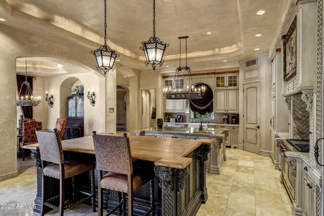 10894 E Turquoise Ave, Scottsdale, AZ 85259 - kitchen featuring a notable chandelier, a center island with sink, a tray ceiling, arched walkways, and decorative backsplash