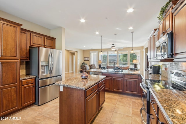 kitchen featuring appliances with stainless steel finishes, light stone counters, sink, a kitchen island, and hanging light fixtures