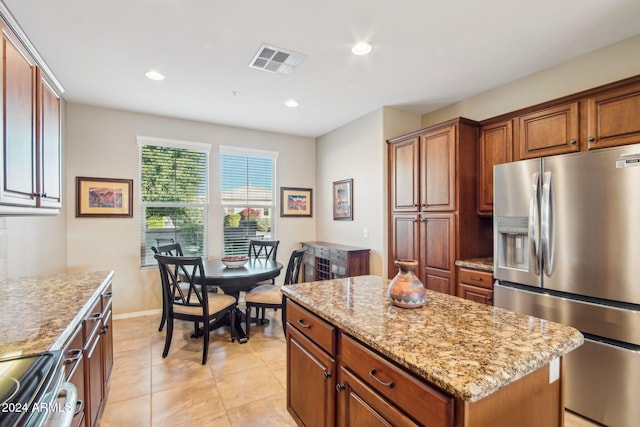 kitchen featuring light stone countertops, stainless steel fridge, range, a kitchen island, and light tile patterned flooring