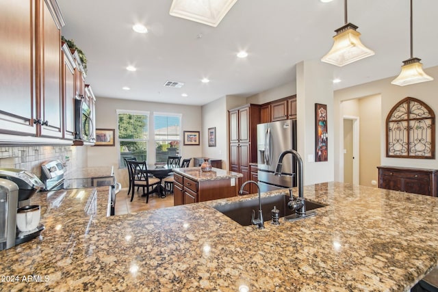 kitchen with sink, hanging light fixtures, light stone countertops, a kitchen island, and stainless steel appliances