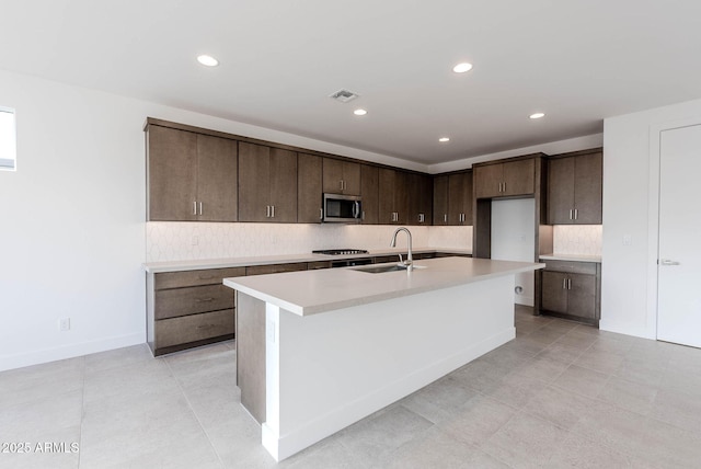 kitchen with dark brown cabinets, appliances with stainless steel finishes, sink, and a center island with sink