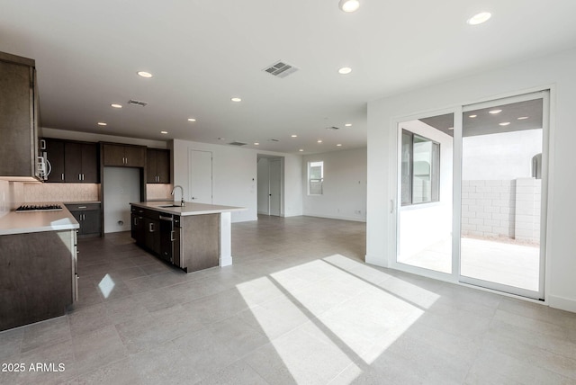 kitchen with tasteful backsplash, sink, a kitchen island with sink, black stovetop, and dark brown cabinets