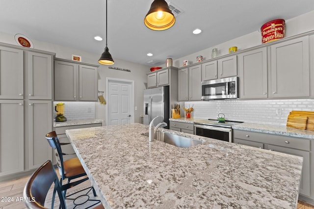 kitchen featuring appliances with stainless steel finishes, a breakfast bar area, light stone countertops, a kitchen island with sink, and a sink