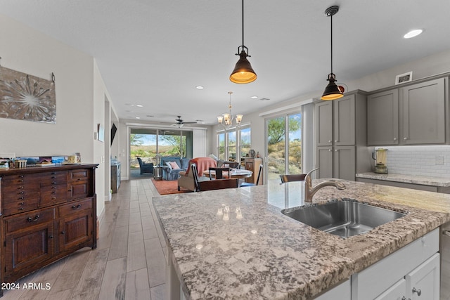 kitchen with tasteful backsplash, light wood-style floors, a kitchen island with sink, a sink, and light stone countertops