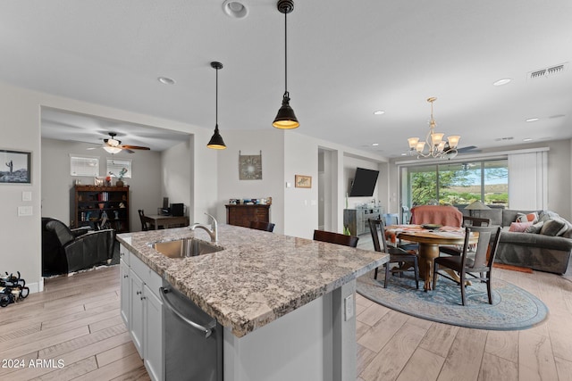 kitchen with a sink, white cabinets, open floor plan, stainless steel dishwasher, and decorative light fixtures