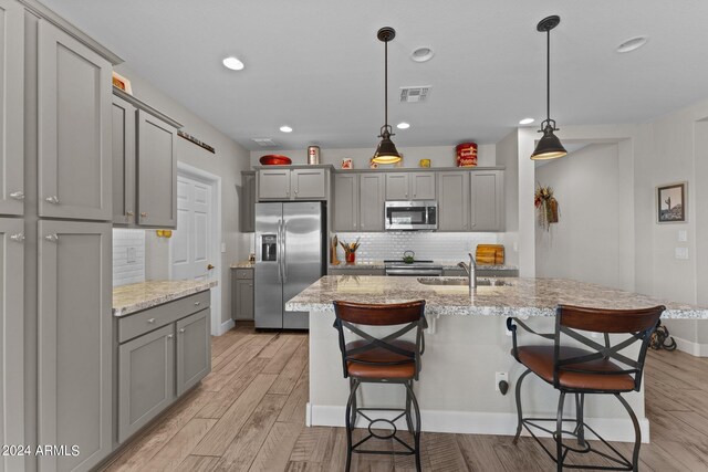 kitchen featuring light stone countertops, hanging light fixtures, stainless steel appliances, gray cabinets, and a center island with sink