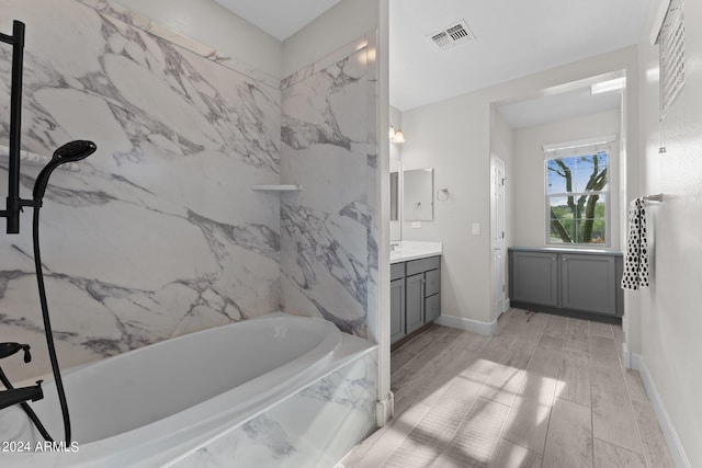 full bath with a tub with marble appearance, vanity, visible vents, and baseboards