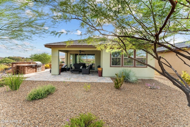 rear view of property featuring an outdoor kitchen, an outdoor hangout area, a ceiling fan, stucco siding, and a patio area