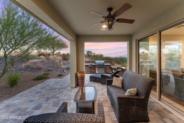 patio terrace at dusk featuring ceiling fan, a grill, an outdoor living space, and exterior kitchen