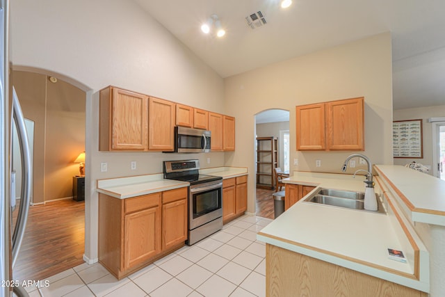 kitchen featuring appliances with stainless steel finishes, high vaulted ceiling, sink, light tile patterned floors, and kitchen peninsula