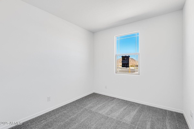 unfurnished room with baseboards and dark carpet