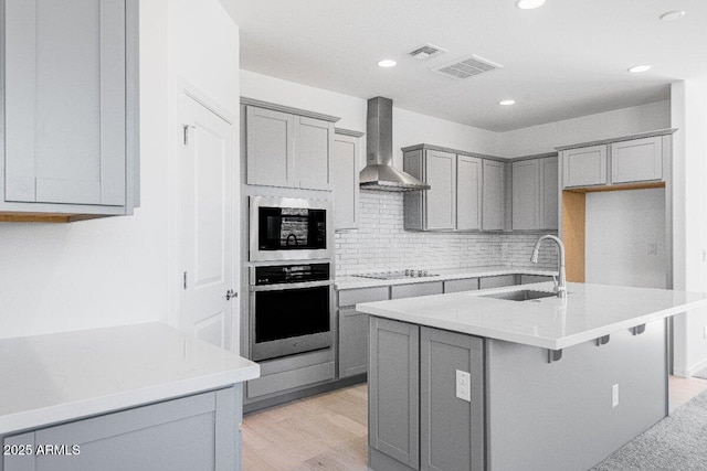 kitchen with wall chimney range hood, a sink, stainless steel oven, and gray cabinetry