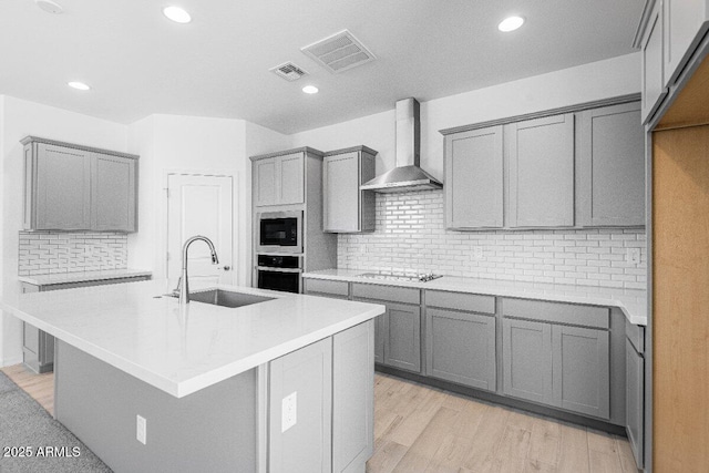 kitchen with gray cabinetry, visible vents, a sink, and wall chimney exhaust hood