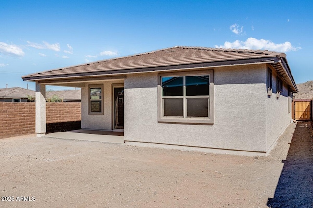 rear view of property featuring a patio, a tile roof, fence, and stucco siding