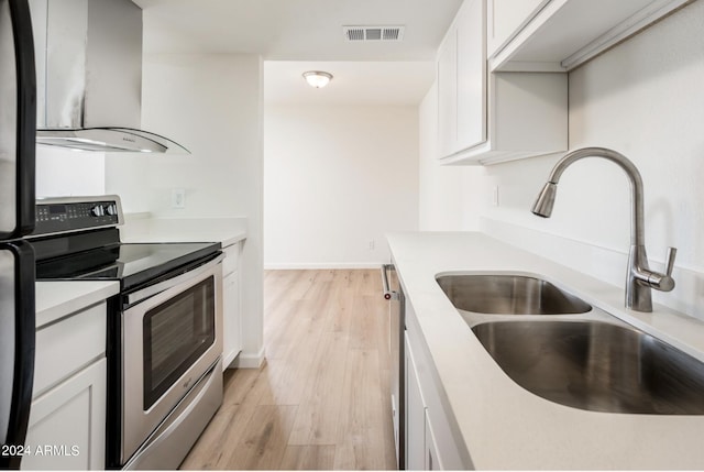 kitchen featuring white cabinets, sink, light wood-type flooring, stainless steel range with electric stovetop, and wall chimney exhaust hood