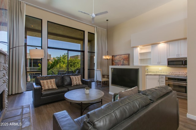 living room featuring dark wood-type flooring, ceiling fan, and a towering ceiling