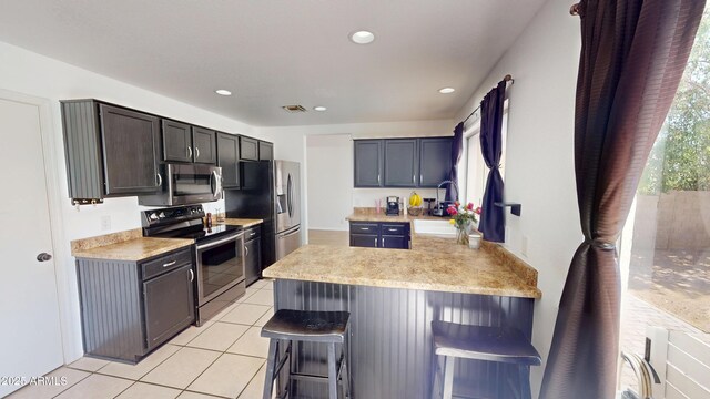 8541 W Pershing Ave, Peoria, AZ 85381 - kitchen featuring appliances with stainless steel finishes, a peninsula, a breakfast bar, light tile patterned floors, and light countertops