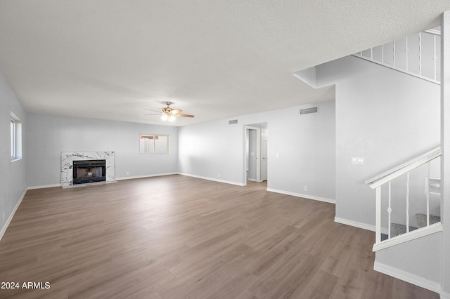 unfurnished living room with ceiling fan, a premium fireplace, and hardwood / wood-style flooring