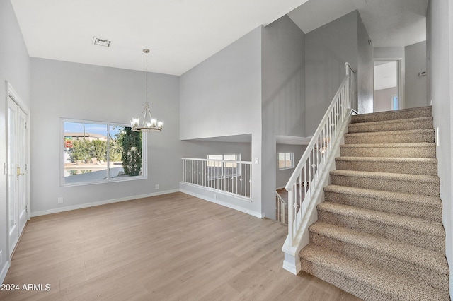 stairs with hardwood / wood-style floors, a high ceiling, and an inviting chandelier