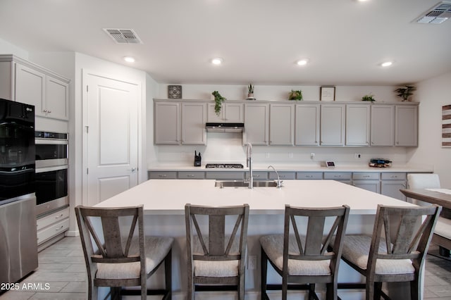 kitchen featuring double oven, sink, gray cabinets, and an island with sink