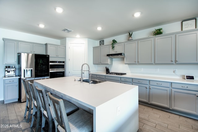 kitchen with sink, gray cabinetry, a center island with sink, a kitchen breakfast bar, and stainless steel appliances