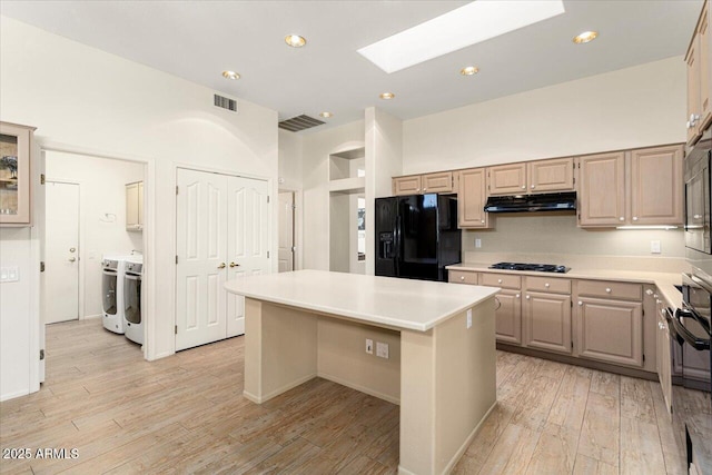 kitchen featuring under cabinet range hood, a kitchen island, light countertops, black refrigerator with ice dispenser, and washing machine and clothes dryer