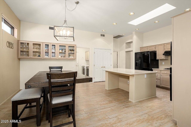 kitchen with glass insert cabinets, a center island, black refrigerator with ice dispenser, light countertops, and a kitchen bar