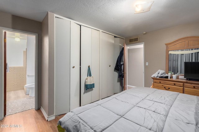 bedroom featuring a closet, ensuite bathroom, a textured ceiling, and light hardwood / wood-style flooring