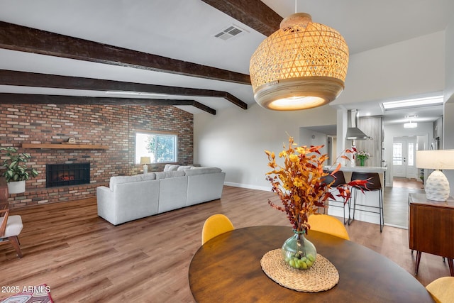 dining space featuring hardwood / wood-style flooring, brick wall, a fireplace, and vaulted ceiling with beams