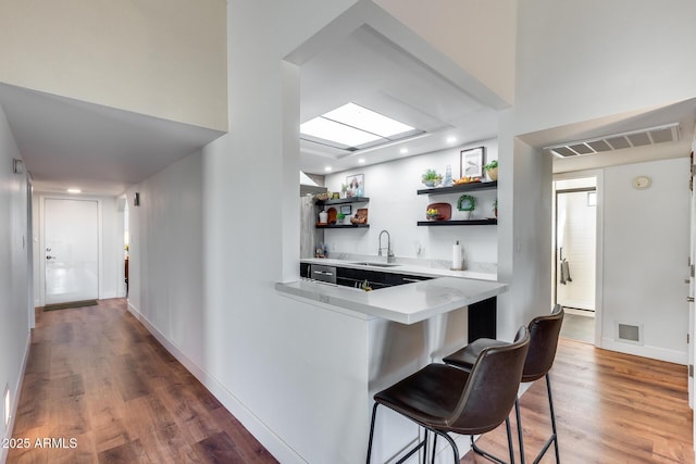 kitchen with kitchen peninsula, a breakfast bar area, wood-type flooring, and sink