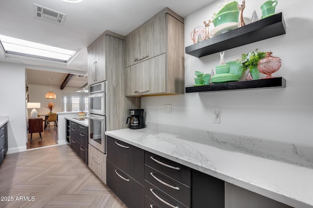 kitchen featuring light stone countertops, light parquet floors, light brown cabinetry, stainless steel double oven, and beamed ceiling