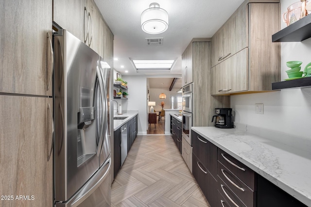 kitchen featuring sink, light stone countertops, a skylight, and stainless steel appliances