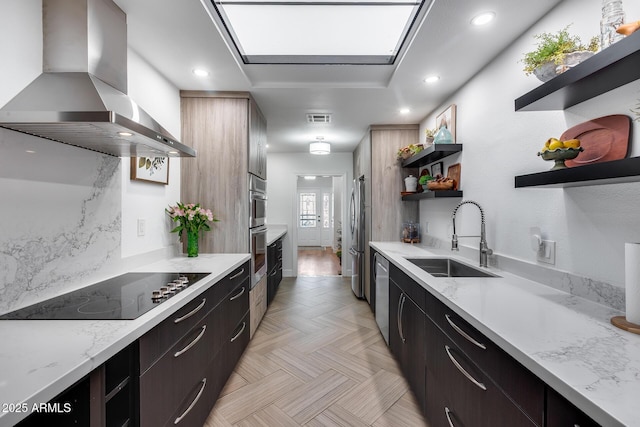 kitchen featuring sink, a skylight, light stone countertops, island range hood, and appliances with stainless steel finishes