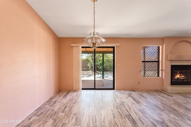 unfurnished dining area featuring baseboards, a tile fireplace, a chandelier, and wood finished floors