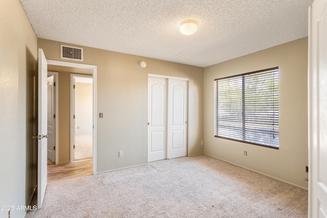 unfurnished bedroom featuring visible vents, baseboards, a closet, a textured ceiling, and carpet flooring