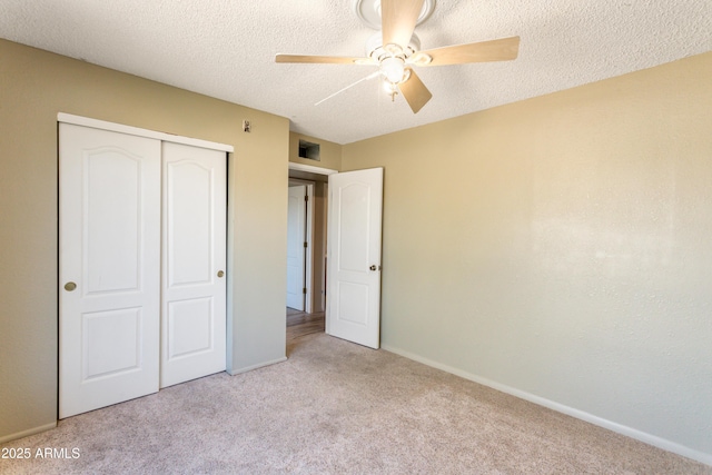 unfurnished bedroom with a closet, baseboards, a ceiling fan, a textured ceiling, and light carpet
