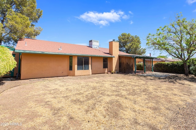 back of house with stucco siding and a chimney