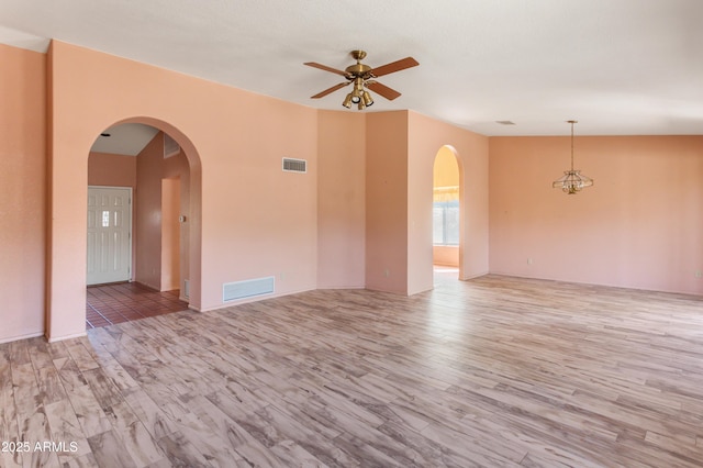 unfurnished room with visible vents, ceiling fan, arched walkways, and wood finished floors