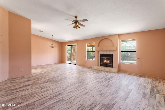 unfurnished living room featuring ceiling fan, visible vents, wood finished floors, lofted ceiling, and a tile fireplace