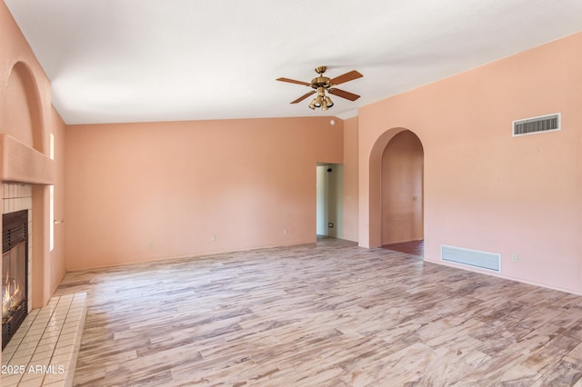 unfurnished living room featuring a tiled fireplace, visible vents, a ceiling fan, and arched walkways