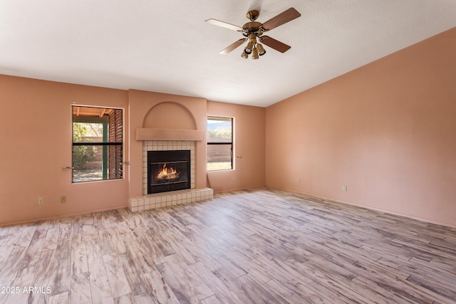 unfurnished living room featuring a wealth of natural light, a tiled fireplace, wood finished floors, and ceiling fan