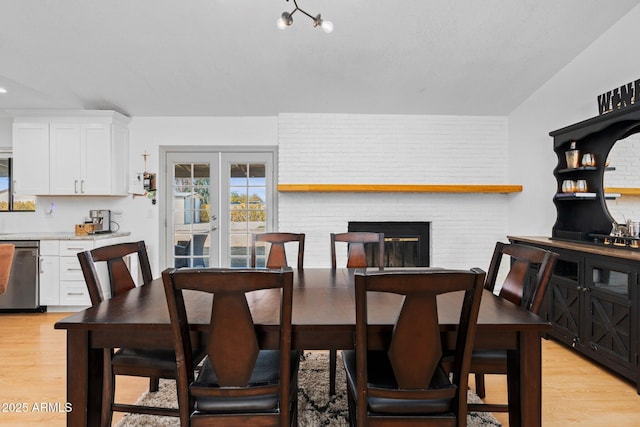 dining space with light hardwood / wood-style flooring, a fireplace, french doors, and brick wall