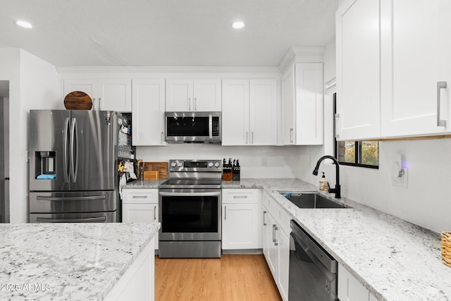 kitchen with sink, light stone countertops, white cabinets, and appliances with stainless steel finishes