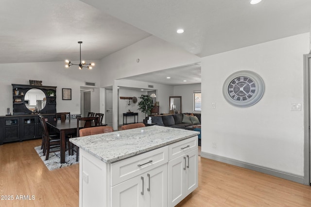 kitchen with a kitchen island, pendant lighting, white cabinetry, lofted ceiling, and a notable chandelier