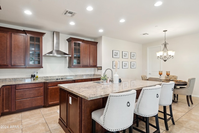 kitchen featuring a breakfast bar area, light stone countertops, sink, a chandelier, and wall chimney range hood