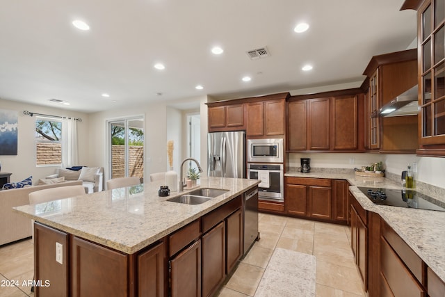 kitchen with stainless steel appliances, sink, light stone countertops, and an island with sink